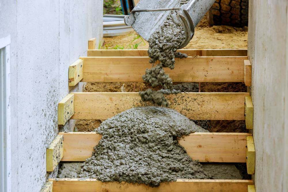 Beton wird aus einer Schütte in die hölzerne Schalung einer Treppe gefüllt.